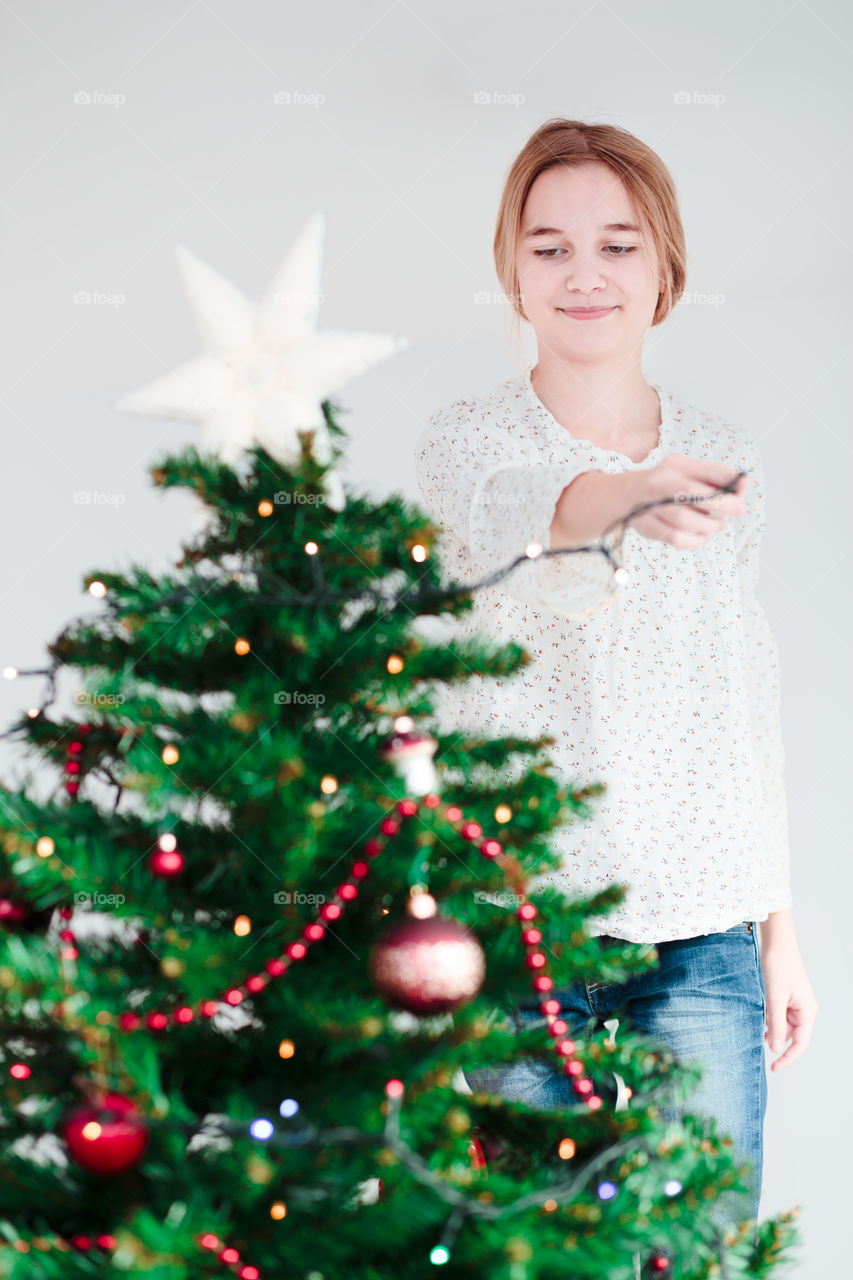 Happy teenage girl decorating christmas tree with lighting equipment