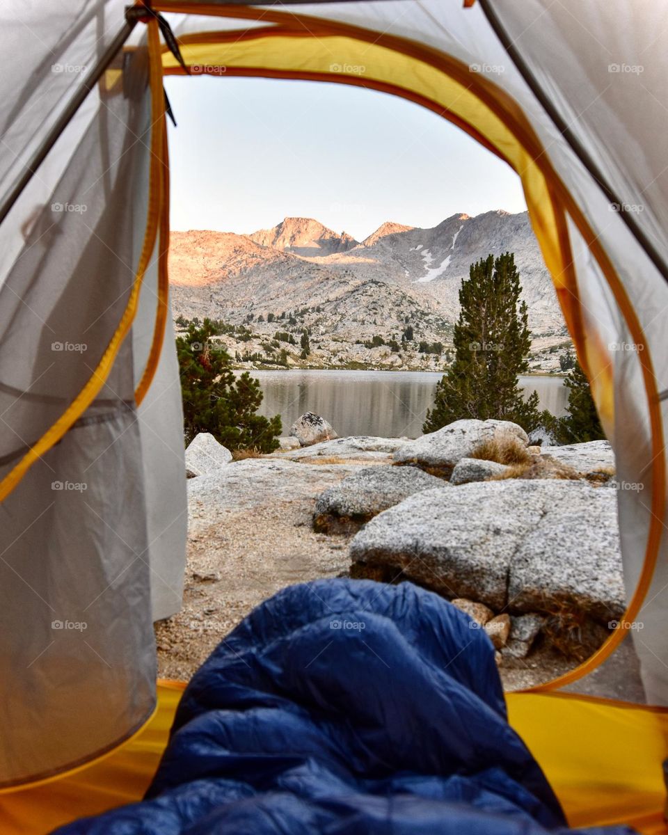 Morning tent views from the sleeping bag shows the sun shining on the mountains and lake.