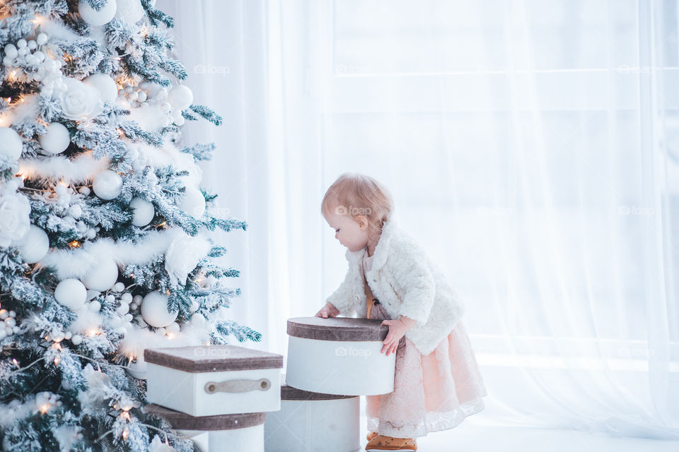 little girl parses New Year gifts at the Christmas tree