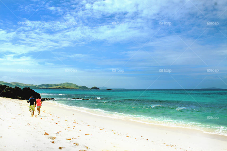 Couple, hand in hand, walking away, leaving footsteps behind, at the beautiful white sand island of Calaguas, Camarines Norte, Philippines