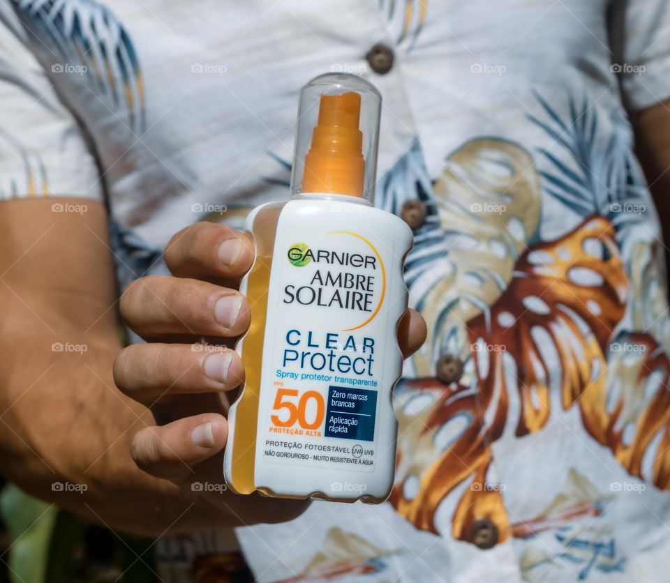 A well tanned man wearing a vintage Hawaiian shirt hold a bottle of Ambre Solaire sun cream