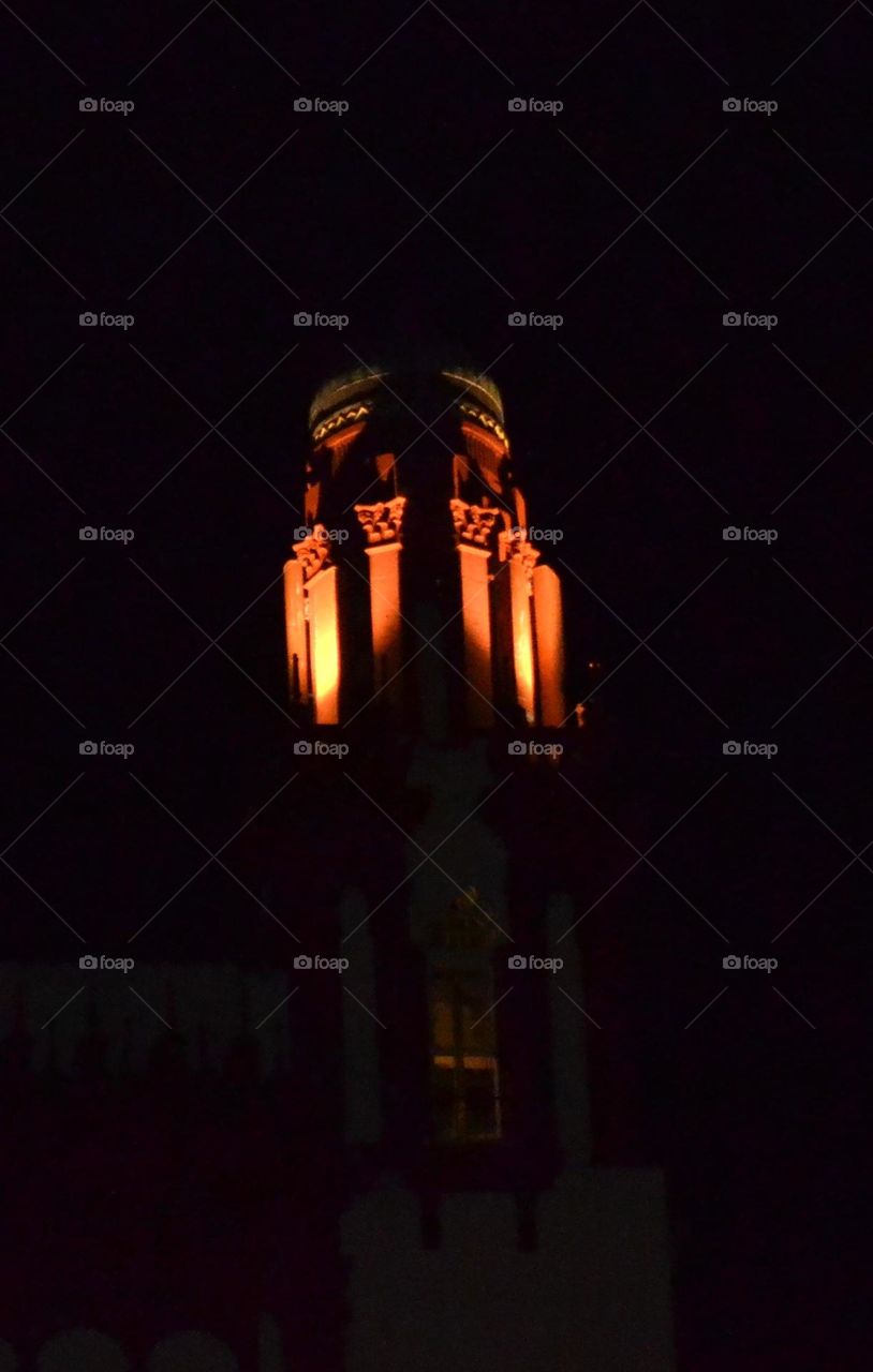 An orange dimly lit ornate turret against a dark black sky a night time