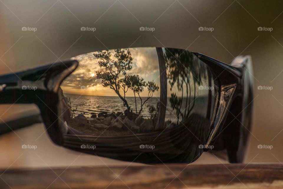 reflection in sunglasses of a peaceful beach scene with palm trees, water and a beautiful orange and blue sunset sky