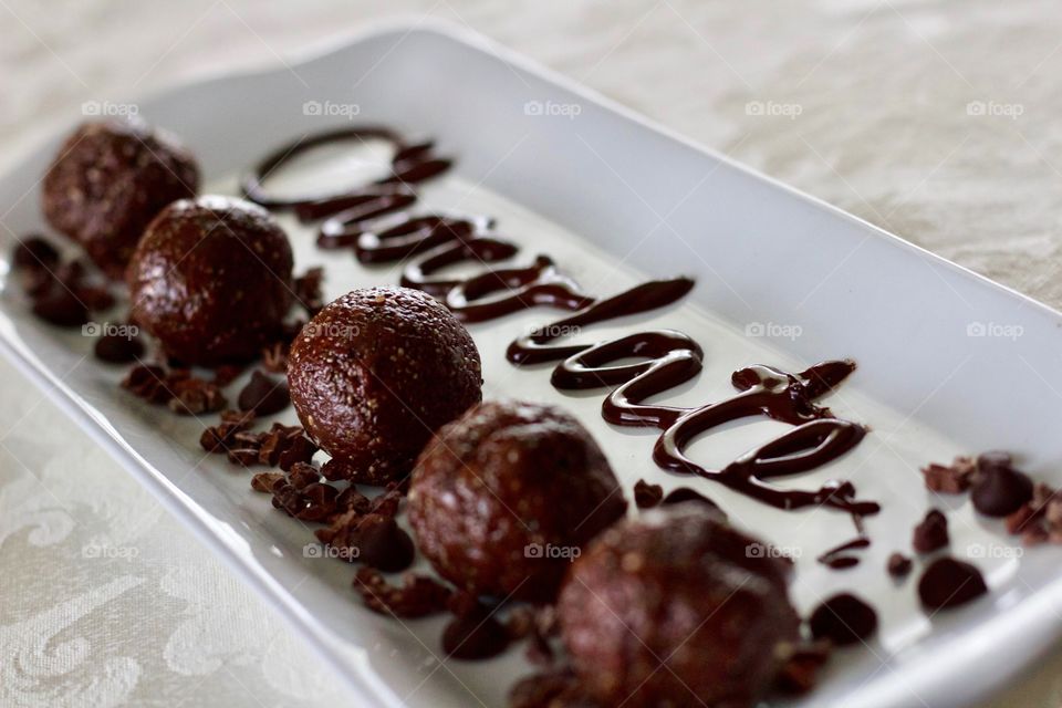 More Chocolate - Nut Butter Cocoa Bites on rectangular white dish with scattered cacao nibs and chocolate chips, and the word "Chocolate" written in chocolate drizzle