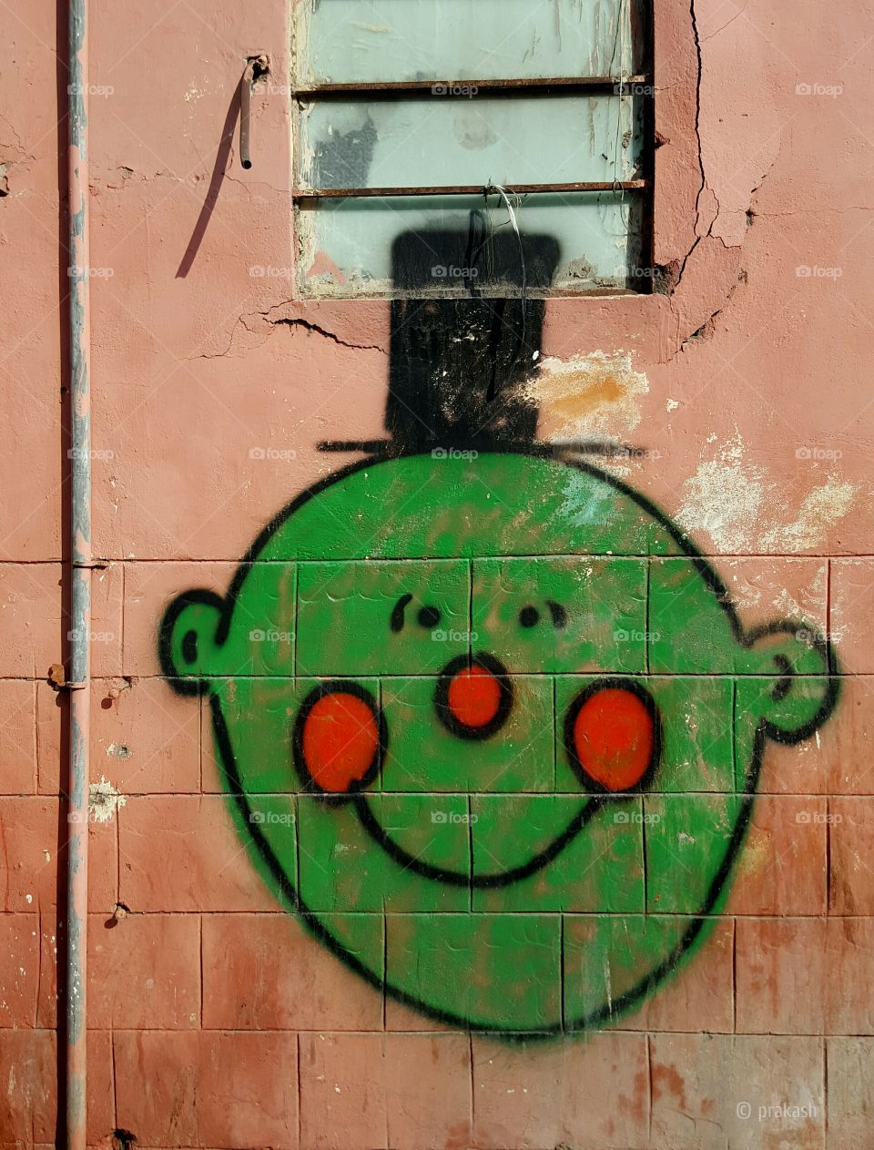 A Smiling Green colored Cartoon creature graffiti painted on a orange wall in the streets of Jaipur India.