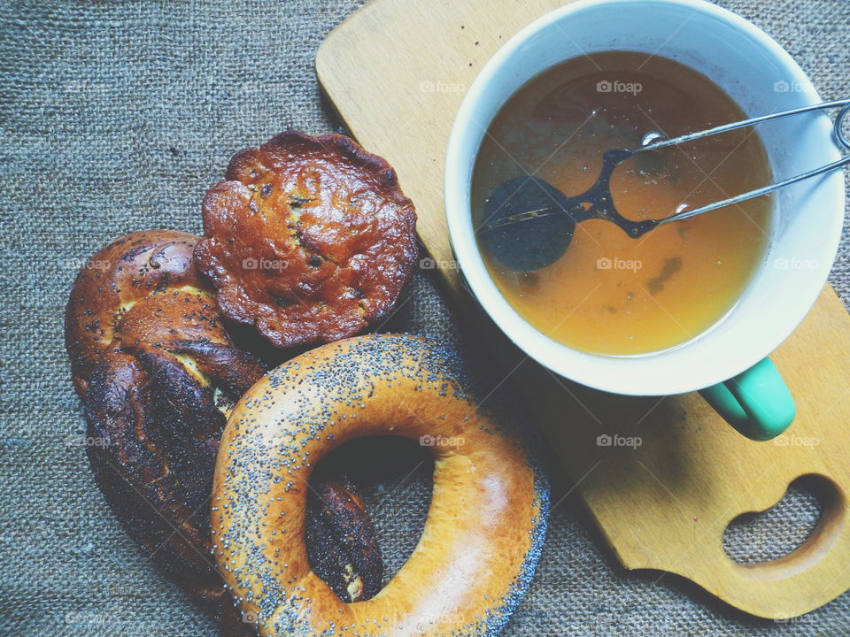 bagel with poppy seeds, basket with poppy seeds, vanilla cupcake and a cup of tea on the table