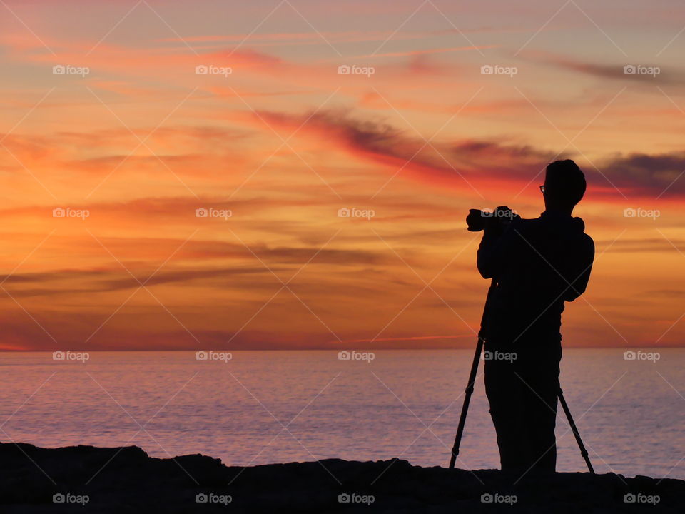 Shadow man takes picture of sunset with tripod 