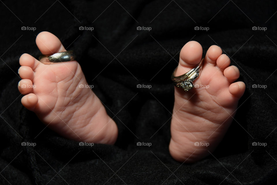 Baby’s feet with wedding rings on big toe, black background.