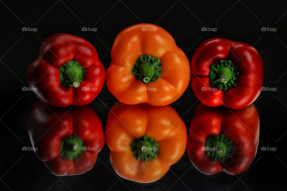three sweet peppers on a black background with reflection