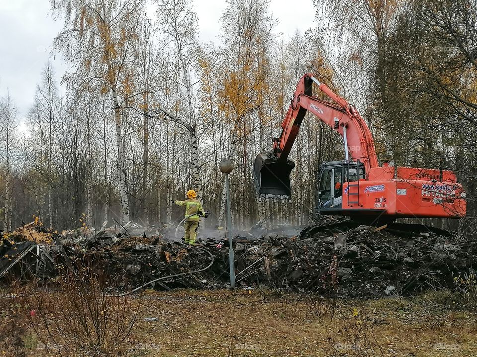 A firefighter and an excavator extinguishing a fire in a large building.
