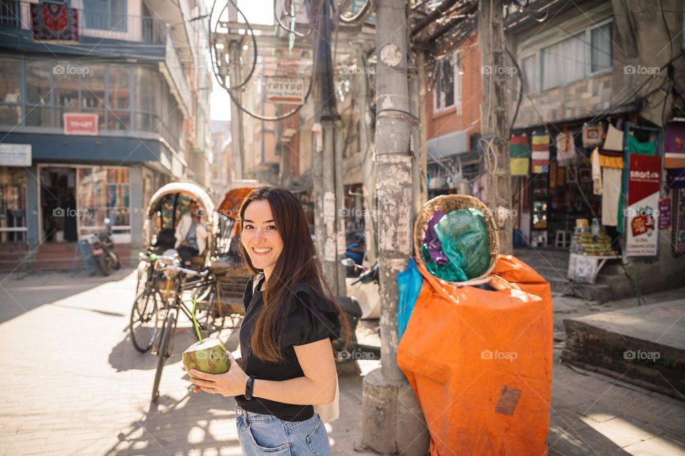 Woman being happy and smiling, holding a fresh coconut on the streets of Kathmanu, Nepal.