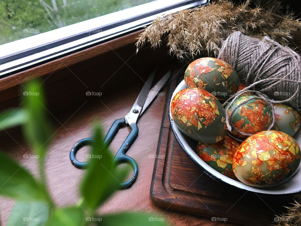 Easter eggs on rustic wooden board and scissors at the window 