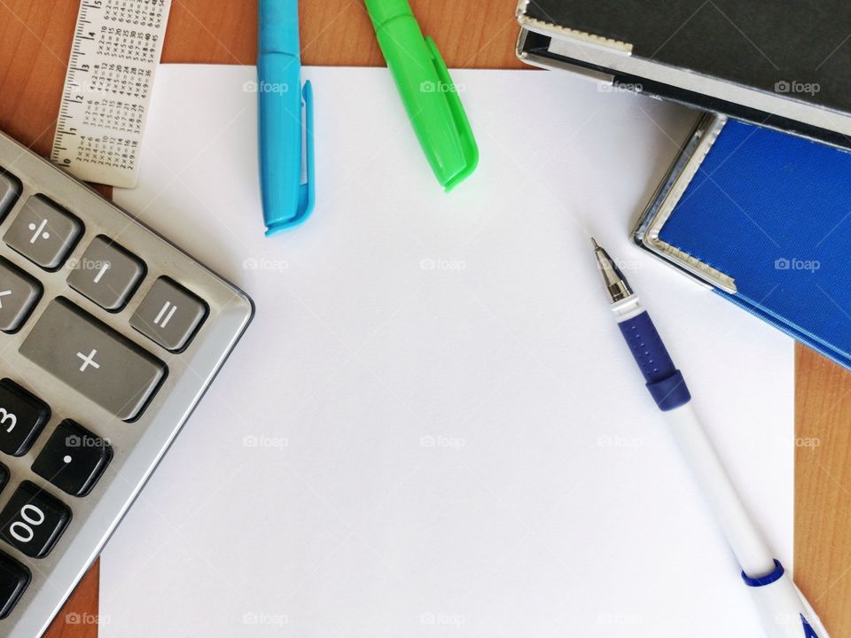 Blank white paper on wooden table with pen, white ruler and calculator from above view