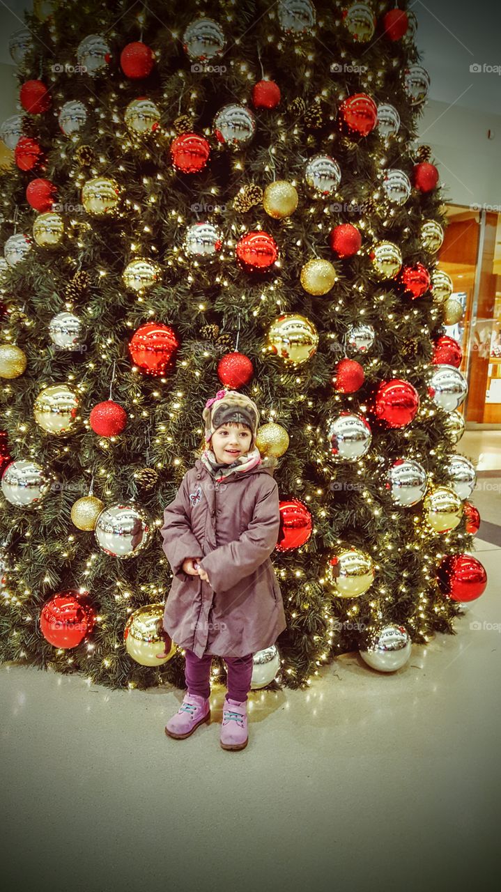 Cute little girl standing in front of christmas tree