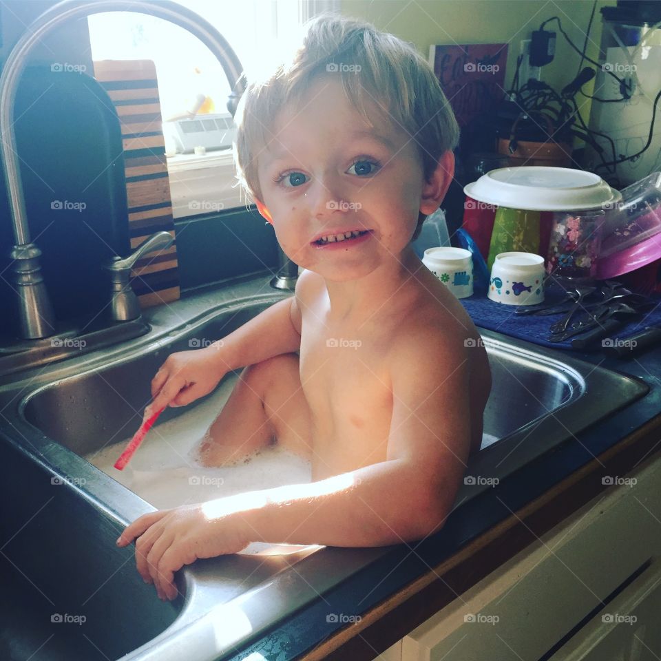 Cute boy sitting in kitchen sink