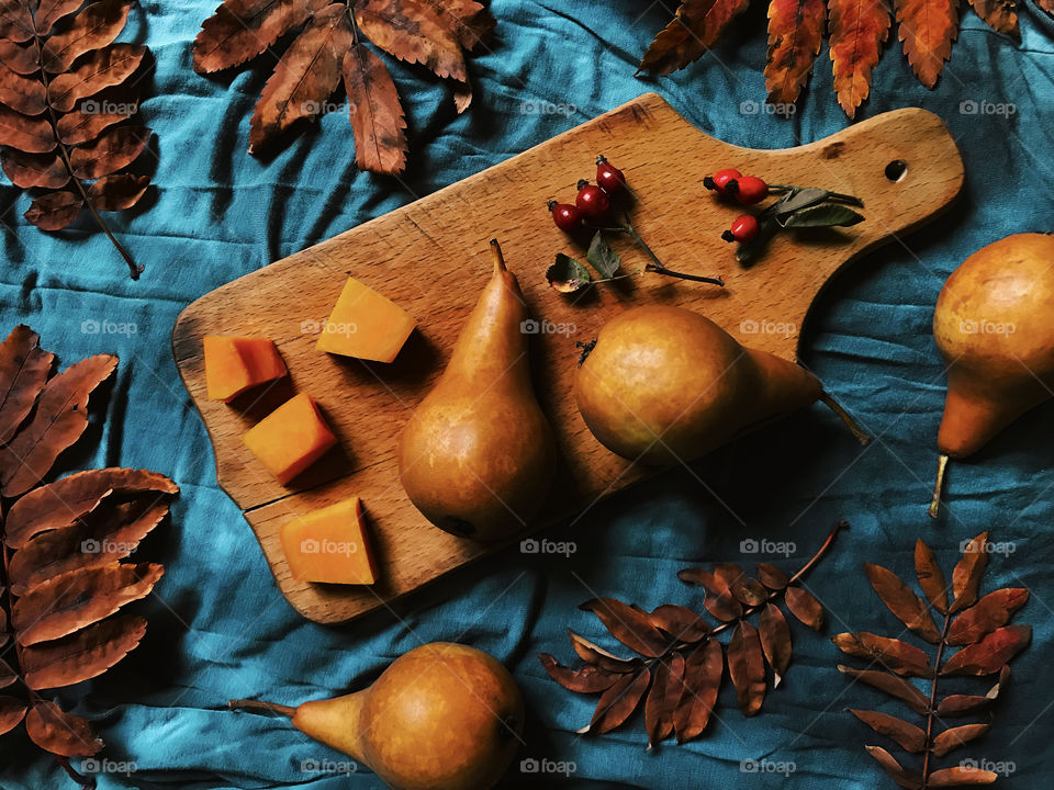 Ripe pears on wooden board with dry autumn leaves and rowan berries 