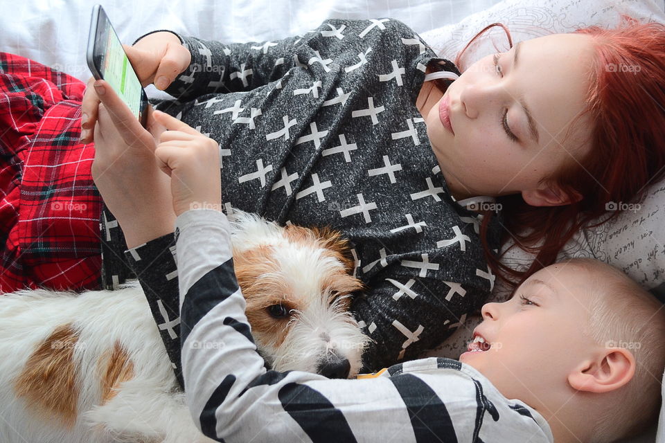 Brother and sister lying on bed with dog