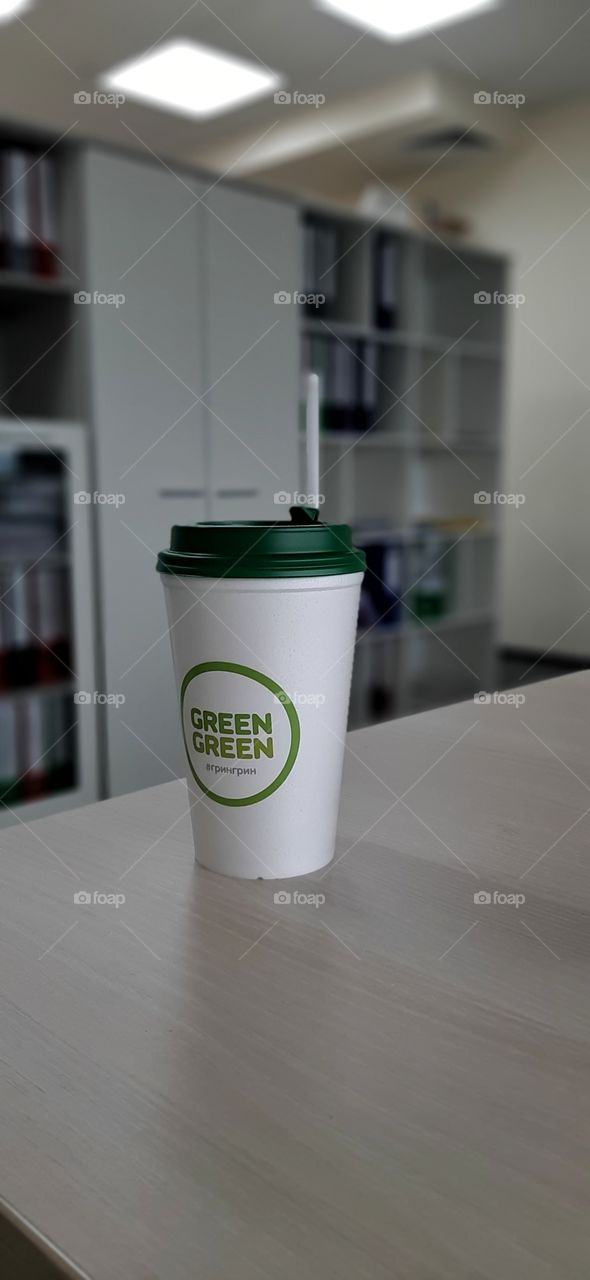 стакан с кофе с зелоной крышкой на столе
