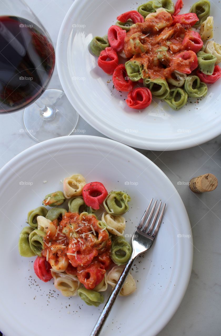 Italian inspired meal of tri-colored tortellini with red sauce and red wine.