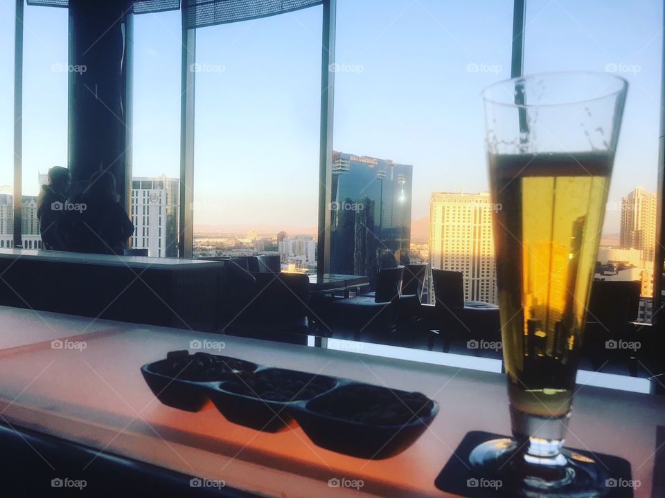 A view of a beer on a bar in front of windows looking out to large buildings in Las Vegas Nevada during a peaceful happy hour 