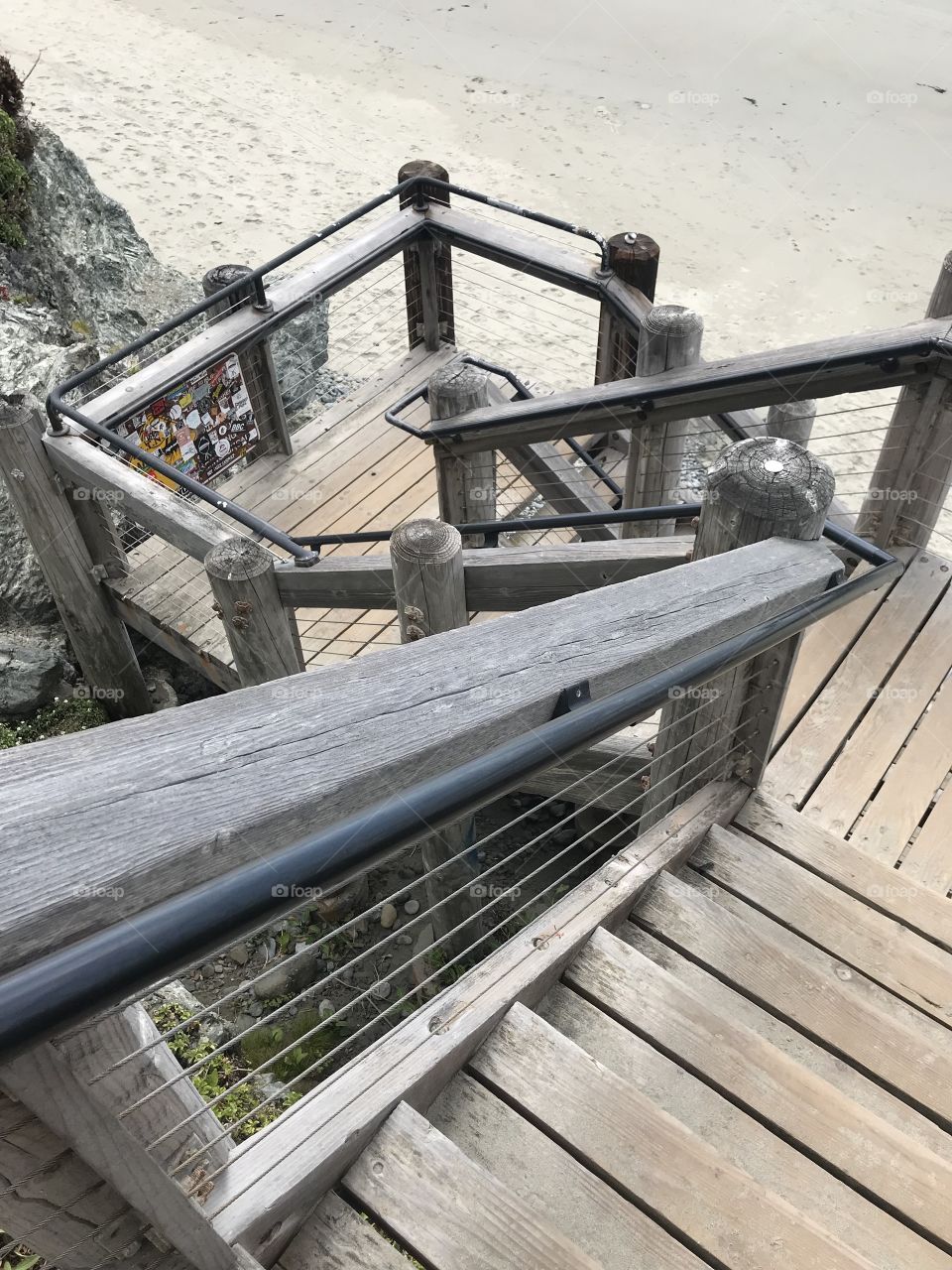 Twisting downwards towards the damp sand of a coastal beach, the staircase’s weathered wood posts and metal rails start to blend into the landscape. 