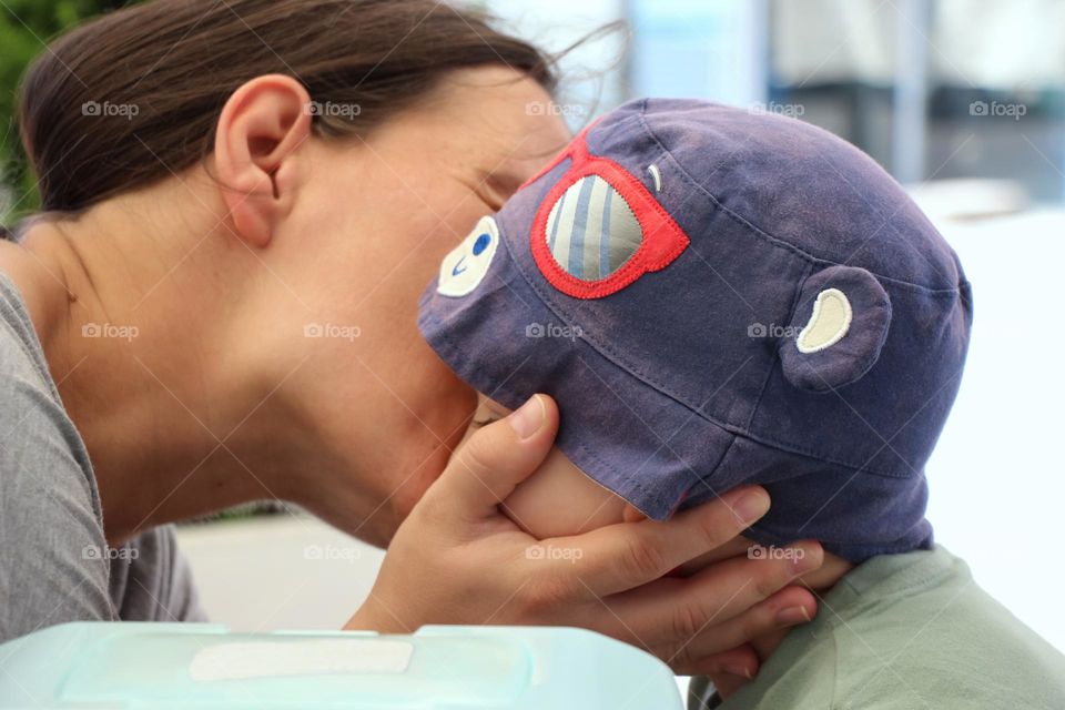 A mom's kissing her son with blue hat