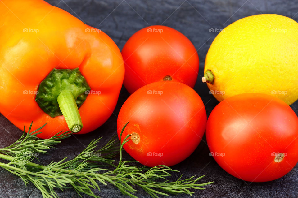 Bright vegetables and fruits (yellow and orange peppers, red tomatoes, yellow lemon, green dill) against the background of an old cracked sun-bleached board. With space for inscription.
