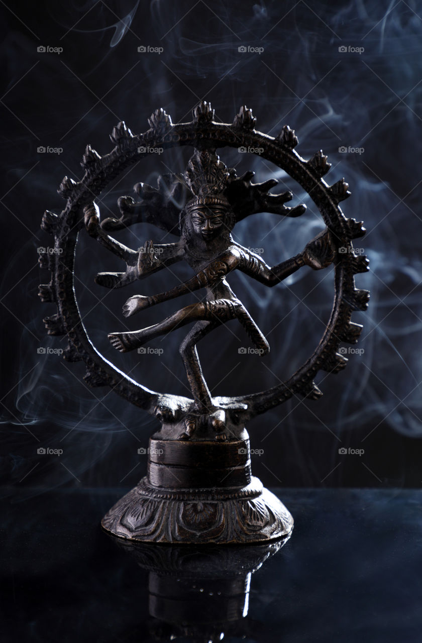 Indian God metal Nataraj Statue on black background with smoke from incense cones