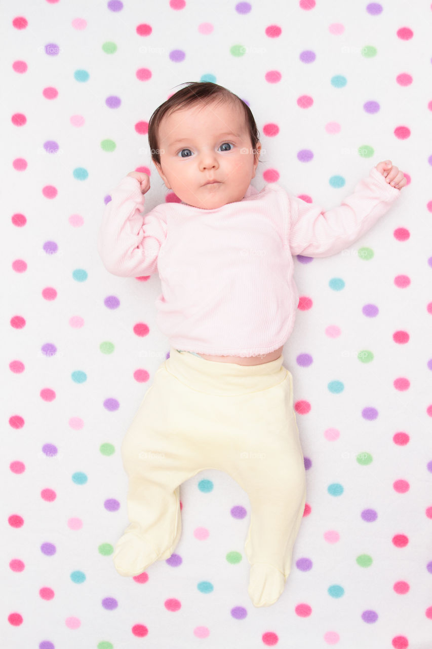 Little baby girl. Top view of little baby lying on blanket with colourful polka dots