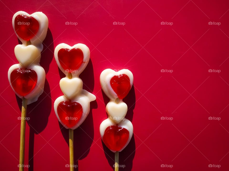 Three sweet red and white Lollipop Candy in the shape of hearts close up on a red background with copy space