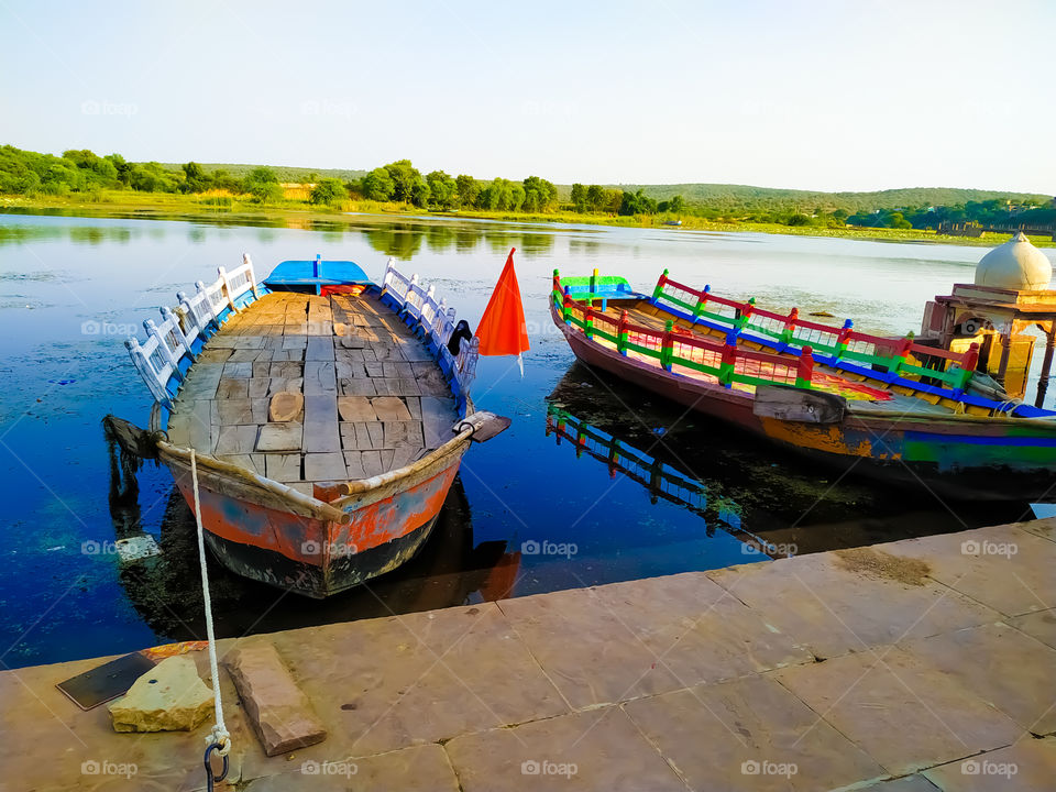 Two wooden boats parked along the river with green trees and green hills in the site behind the river