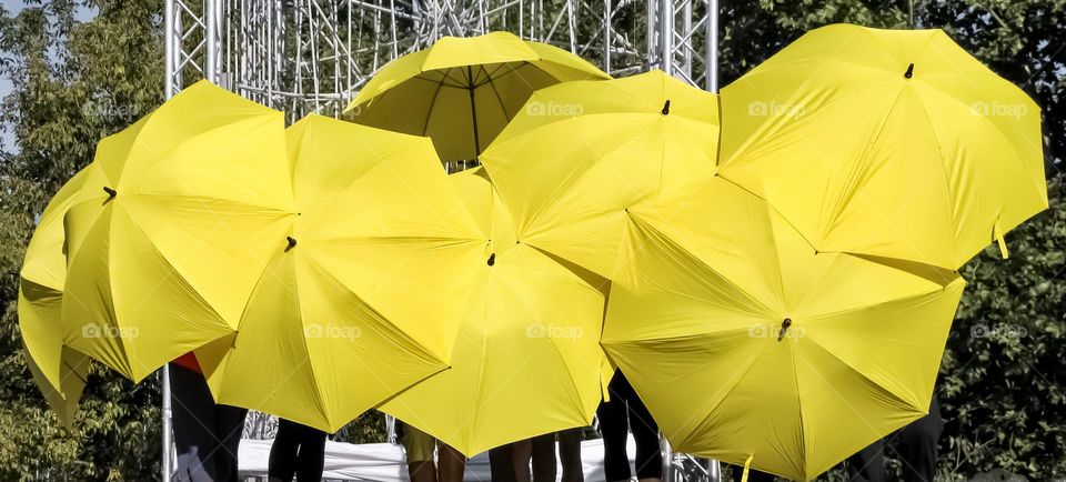 Performers hide behind yellow umbrellas made up of triangular shapes