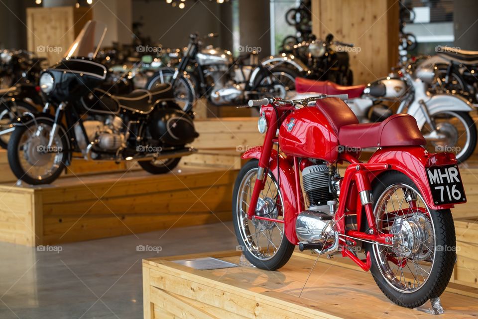 Old restored motorcycles. Old red restored motorcycle in the foreground. Several black and silver bikes in the background. On top of wooden boxes