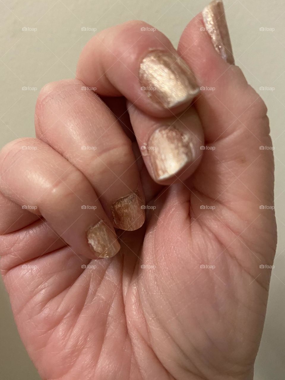 A photo of a fist with gold painted fingernails against an off-white background and with fingers crossed. 