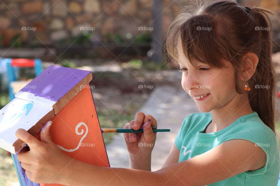 Child painting a wooden bird house