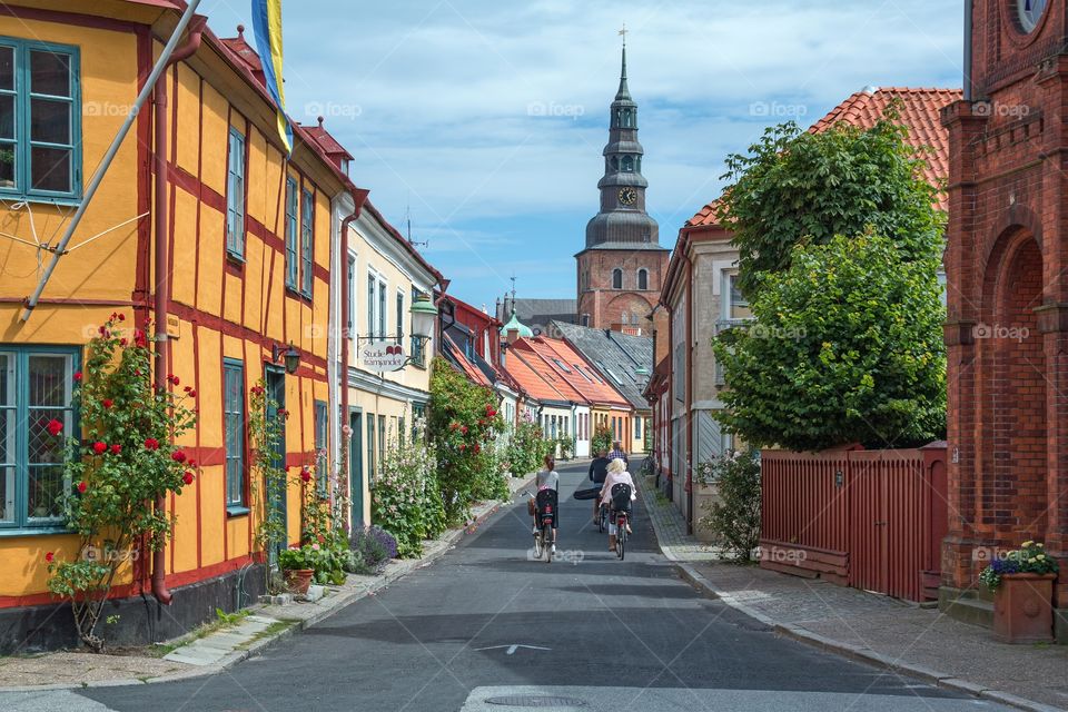  Cyclists on Lilla Västergatan in Ystad, Österlen, Sweden, with Sankta Maria church in the background.