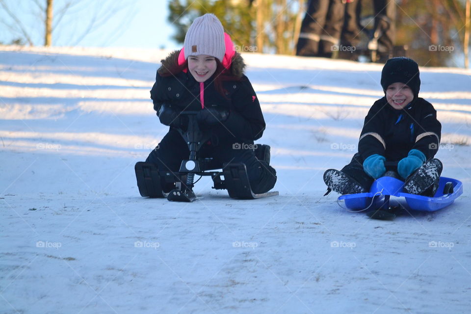 Two children racing down the hill with sleds