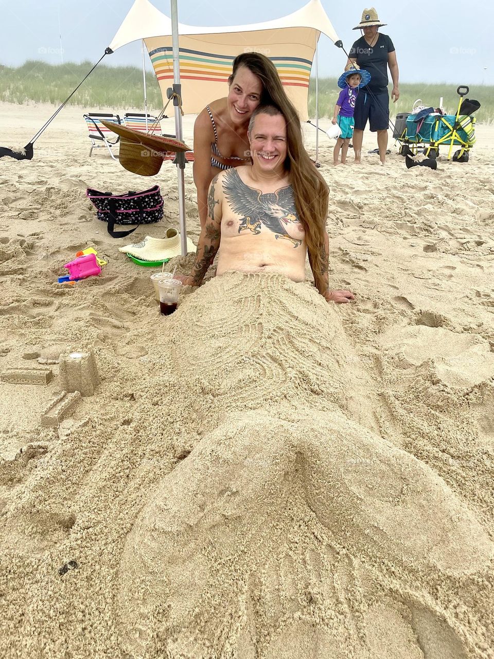 Man on the beach buried in sand as a mermaid, man mermaid at the beach, making a mermaid at the beach, turning people into mermaids