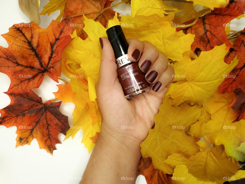 Holding a fall color nail polish with colorful faux fall leaves in the background.