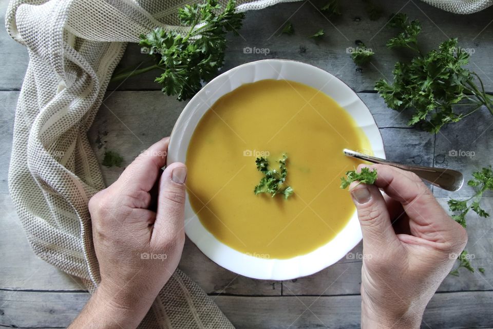 Man eating butternut squash soup sprinkling parsley on top with wood background