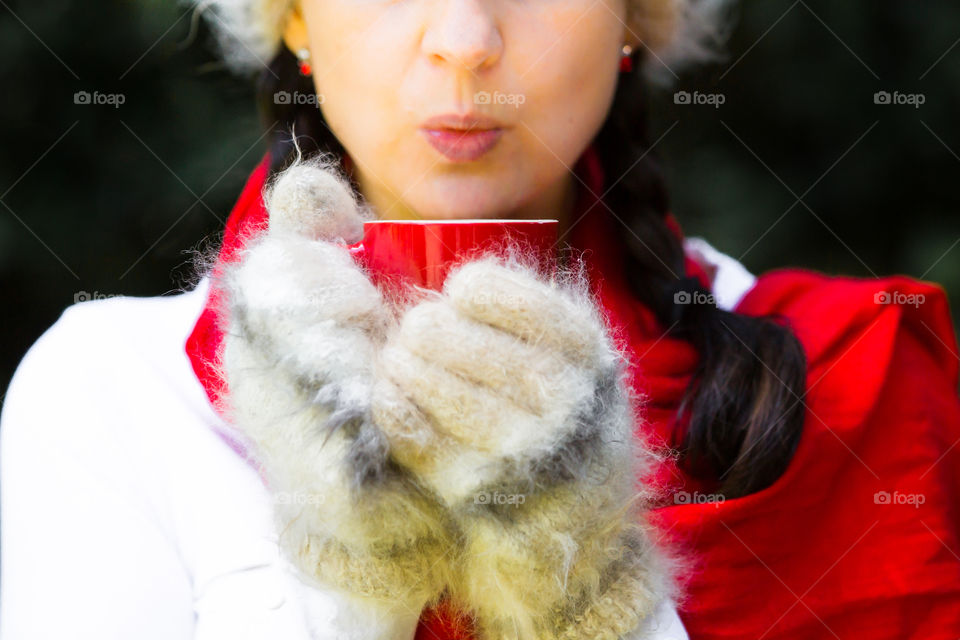 Love coffee on a cold day - image of woman blowing on a warm drink in red cup with mohair gloves and red scarf