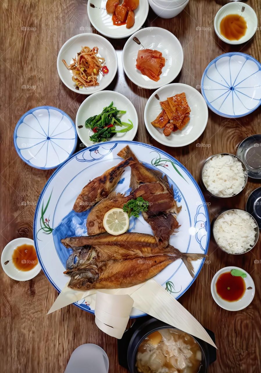 a fried fish, kimchi,two bowl of rice, bean paste soup, spicy friend vegetables and etc.