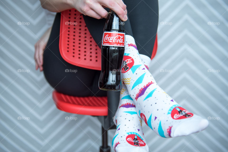 Person sitting with legs hanging over a chair and holding a bottle of Coca-cola