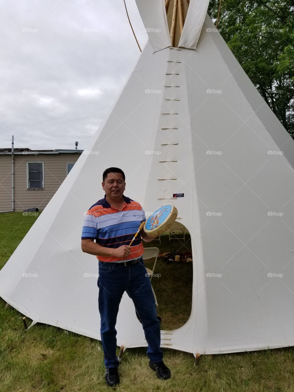 first nation man drums beside his teepee.