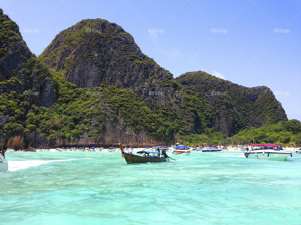 Many boats swimming in blue clear sea water at the tropical beach with mountains 