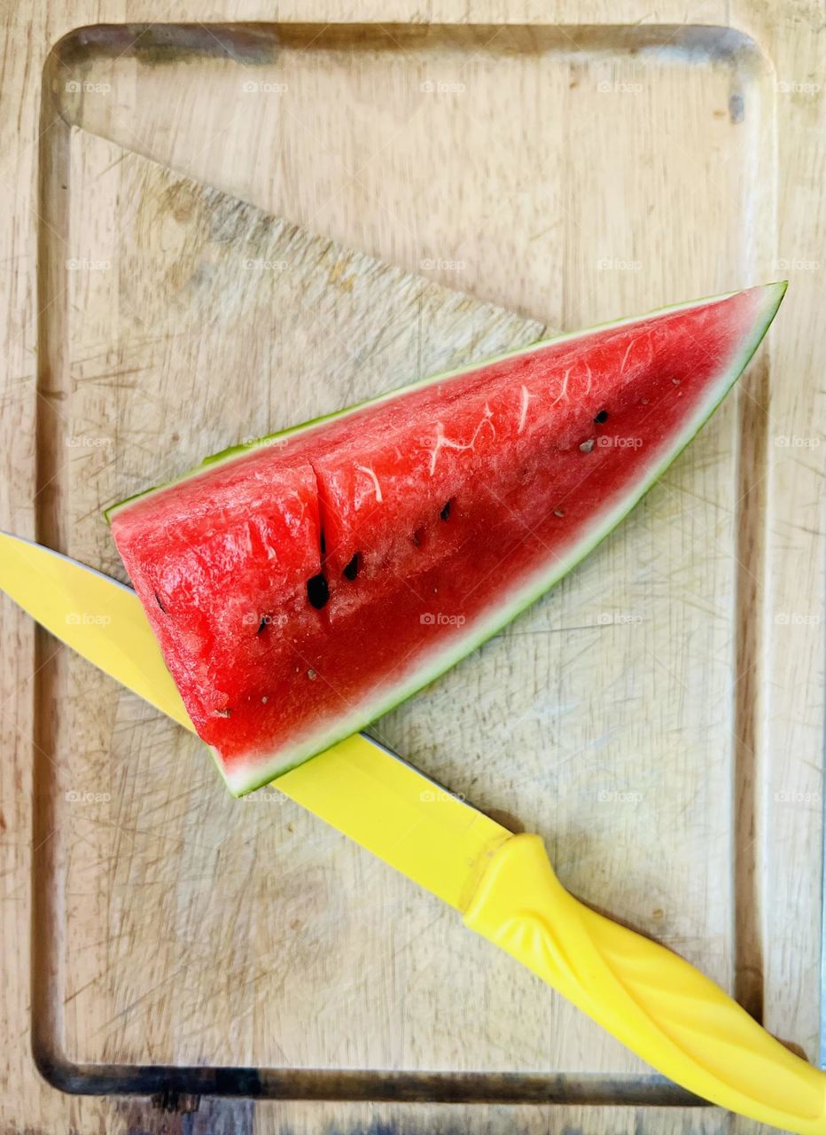 A slice of watermelon and a yellow knife in the kitchen 
