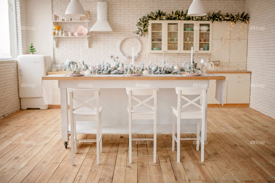 Festive winter cozy kitchen interior with garlands, decorations and gifts.  Christmas dinner at the decorated table.