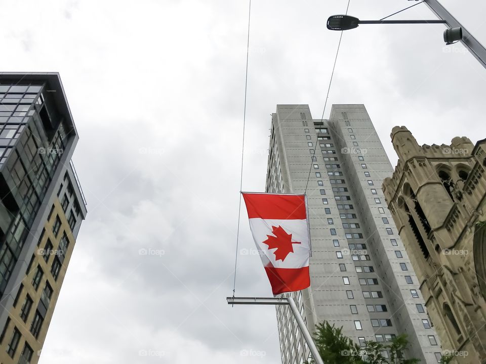 Canadian flag flying in downtown Montreal, Canada next to historic buildings and modern sky rise office buildings low angle view looking up  on a cloudy day with vibrant red and white flag colors in contrast 