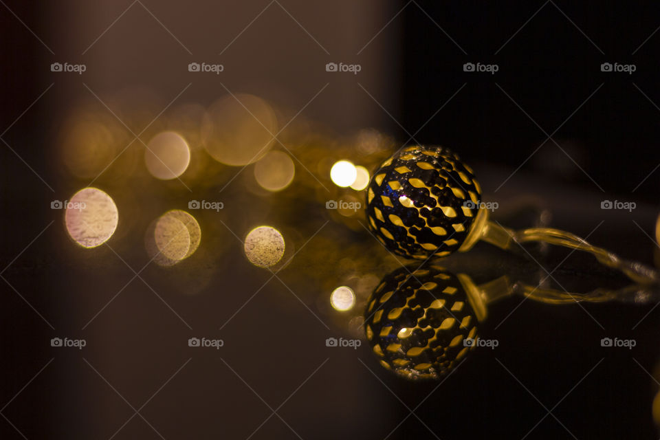 A portrait of some light ornament lying on a black reflective surface with bokeh balls in the background.