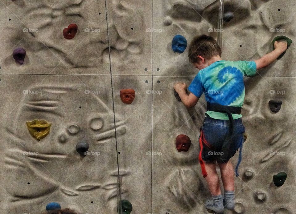 Boy In Rock Climbing Gear. Young Boy Climbing A Rock Wall
